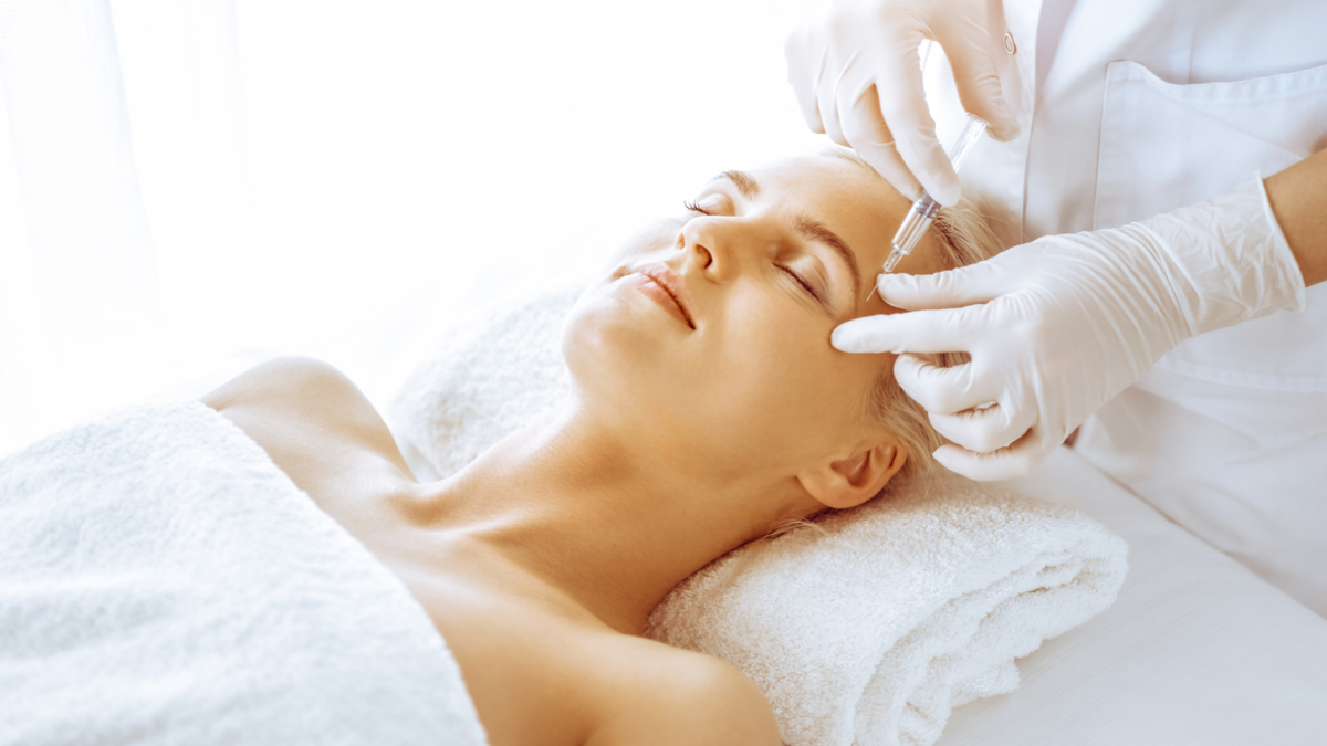 Beautician doctor hands doing beauty procedure to female blonde face with syringe in clinic. Cosmetic medicine and surgery, beauty injections concept.